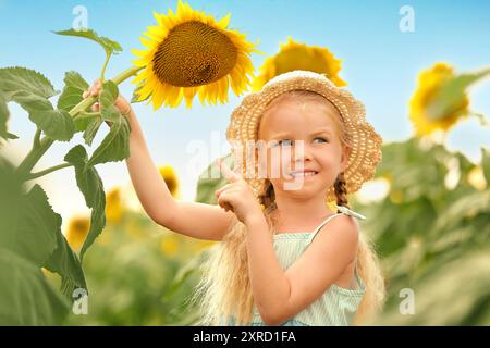 Süßes kleines Mädchen, das auf Sonnenblume im Feld zeigt Stockfoto