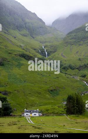 Glencoe, Schottland, Großbritannien. Juli 2024. Ferienhaus unter einem Wasserfall mit grünen Feldern und Schafweiden. Glencoe ist ein Dorf im Westen Schottlands. Er liegt im steilen Glencoe Valley in den schottischen Highlands. Die Gegend ist bekannt für Wasserfälle und Wanderwege, die Gipfel wie Buachaille Etive Mor und Bidean nam Bian erklimmen. Glencoe, ein ausgewiesenes National Scenic Area, das manchmal auch als „Glen of Weeping“ bezeichnet wird, war Schauplatz des berüchtigten „Massakers von Glencoe“ im Jahr 1692. (Kreditbild: © Ruaridh Stewart/ZUMA Press Press Wire) NUR REDAKTIONELLE VERWENDUNG! Nicht für kommerzielle ZWECKE! Stockfoto