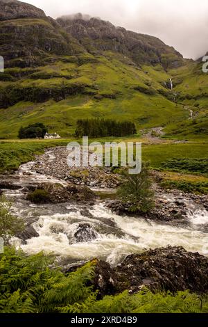 Glencoe, Schottland, Großbritannien. Juli 2024. Ferienhaus unter einem Wasserfall mit grünen Feldern und Schafweiden. Glencoe ist ein Dorf im Westen Schottlands. Er liegt im steilen Glencoe Valley in den schottischen Highlands. Die Gegend ist bekannt für Wasserfälle und Wanderwege, die Gipfel wie Buachaille Etive Mor und Bidean nam Bian erklimmen. Glencoe, ein ausgewiesenes National Scenic Area, das manchmal auch als „Glen of Weeping“ bezeichnet wird, war Schauplatz des berüchtigten „Massakers von Glencoe“ im Jahr 1692. (Kreditbild: © Ruaridh Stewart/ZUMA Press Press Wire) NUR REDAKTIONELLE VERWENDUNG! Nicht für kommerzielle ZWECKE! Stockfoto