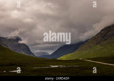 Glencoe, Schottland, Großbritannien. Juli 2024. Blick hinunter auf Glencoe vorbei an Autos auf der A82 mit hoch aufragenden Bergen und Sturmwolken. Glencoe in den westlichen schottischen Highlands. Die Gegend ist bekannt für Wasserfälle und Wanderwege, die Gipfel wie Buachaille Etive Mor und Bidean nam Bian erklimmen. Glencoe, ein ausgewiesenes National Scenic Area, das manchmal auch als „Glen of Weeping“ bezeichnet wird, war Schauplatz des berüchtigten „Massakers von Glencoe“ im Jahr 1692. (Kreditbild: © Ruaridh Stewart/ZUMA Press Press Wire) NUR REDAKTIONELLE VERWENDUNG! Nicht für kommerzielle ZWECKE! Stockfoto