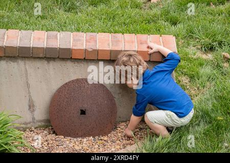 Der zweijährige kaukasische Kleinkinder spielt im Hof mit Kieselsteinen. Stockfoto