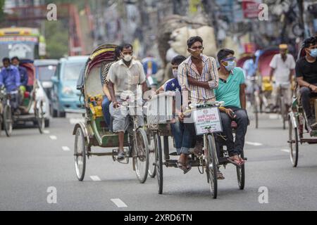 Ein Rikscha-wala oder ein Rikscha-Fahrer mit seinen Passagieren auf den Straßen von Dhaka. Die Bewohner der Hauptstadt Dhaka in Bangladesch stellen sich der Bedrohung durch den Corona-Virus COVID 19. Stockfoto