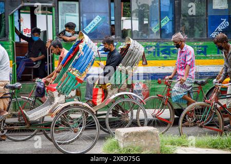 Ricksha-walas, oder Rikscha-Fahrer mit ihren Passagieren auf den Straßen von Dhaka. Die Bewohner der Hauptstadt Dhaka in Bangladesch stellen sich der Bedrohung durch den Corona-Virus COVID 19. Stockfoto