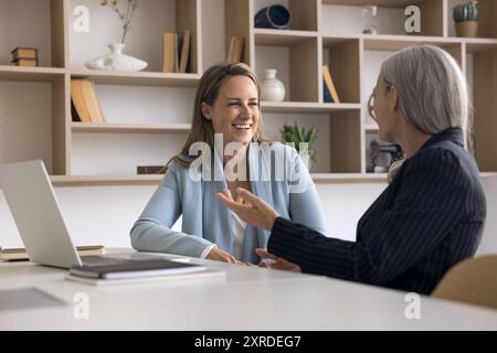 Zwei positive jüngere und ältere Geschäftsfrauen sprechen am Arbeitsplatz Stockfoto