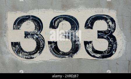 Ein abgenutztes Schild mit der Nummer 333 auf einer Betonwand Stockfoto