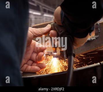 Nahaufnahme eines professionellen Ingenieurs beim Schneiden von Metall mit Brenner. Bei extremer Hitze, die auf den Stahl angewendet wird, entstehen Funken an einer industriellen Arbeitsstätte. Stockfoto