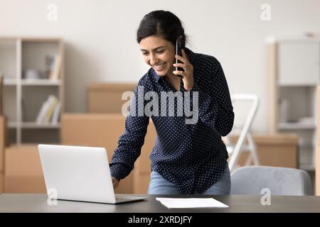 Indische Frau, Lagerarbeiter, die einen Laptop benutzt, während sie telefoniert Stockfoto
