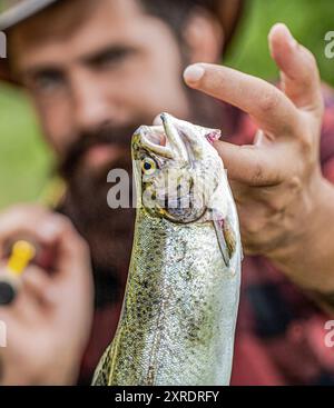 Fischer und Trophäenforelle. Fischer mit Rute und Fisch. Mann fischt auf dem Fluss. Fischer mit Angelrute in der Hand, der Fische aus dem Fluss zieht. Mann Stockfoto