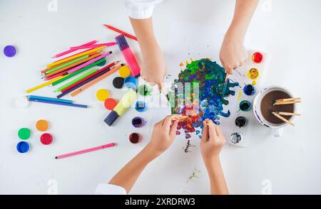 Kreatives Kunstkonzept mit bunten Farben auf weißem Papier. Die Hände des kleinen Kindes zeichnen Aquarelle auf Papier am Tisch. Kinderhände malen im Stockfoto