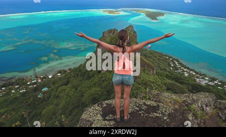 Junge Touristen stehen auf einem Berggipfel. Arme ausgestreckt. Genießen Sie den Blick auf eine tropische Insel mit einer türkisfarbenen Lagune darunter Stockfoto