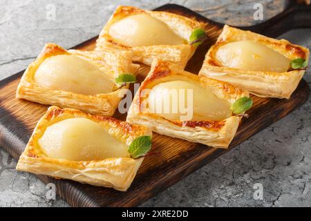 Köstliche hausgemachte pochierte Birnen in Blätterteig aus der Nähe auf dem Holzbrett auf dem Tisch. Horizontal Stockfoto