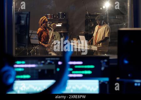 Musiker, die in einem professionellen Aufnahmestudio Live-Musik produzieren, umgeben von Geräten, die einen vielfältigen Sound erzeugen Stockfoto
