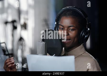 Afroamerikaner, der Kopfhörer trägt und in das Mikrofon singt, während er ein Papier in der Hand hält Stockfoto