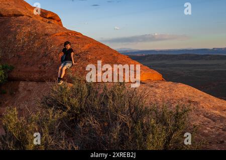 Ein kleiner Junge wandert auf dem Devils Garden Trail bei Sonnenuntergang im Arches National Park, Utah. Das goldene Stundenlicht taucht die rote Felsenlandschaft auf, Kreatin Stockfoto