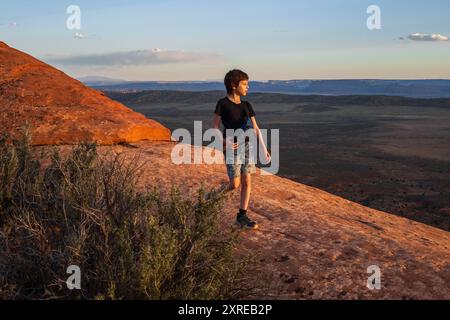 Ein kleiner Junge wandert auf dem Devils Garden Trail bei Sonnenuntergang im Arches National Park, Utah. Das goldene Stundenlicht taucht die rote Felsenlandschaft auf, Kreatin Stockfoto