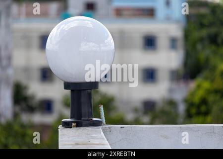 Weiße runde Glaslampe auf einem schwarzen Stahlmast an der weißen Wand auf dem Dach des Hauses, unscharfer Hintergrund. Stockfoto