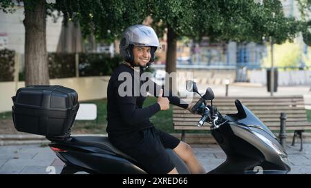 Ein Mann sitzt auf einem Motorrad mit Helm. Er gibt ein Schild mit den Daumen hoch Stockfoto