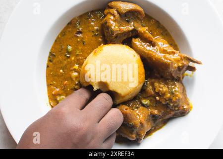 Blick von oben auf nigerianische Ogbono-Suppe und eba auf einem weißen Teller, Blick von oben auf Ogbono-Suppe mit garri und verschiedenen Fleischsorten auf einem Suppenteller Stockfoto