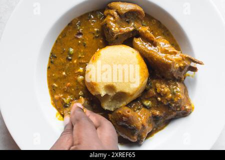 Blick von oben auf nigerianische Ogbono-Suppe und eba auf einem weißen Teller, Blick von oben auf Ogbono-Suppe mit garri und verschiedenen Fleischsorten auf einem Suppenteller Stockfoto