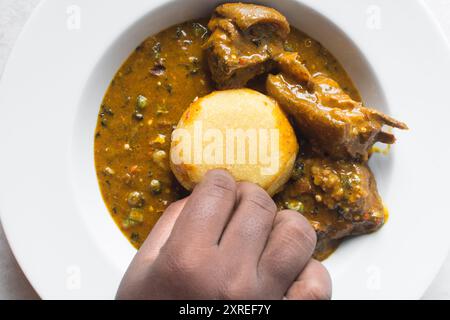 Blick von oben auf nigerianische Ogbono-Suppe und eba auf einem weißen Teller, Blick von oben auf Ogbono-Suppe mit garri und verschiedenen Fleischsorten auf einem Suppenteller Stockfoto