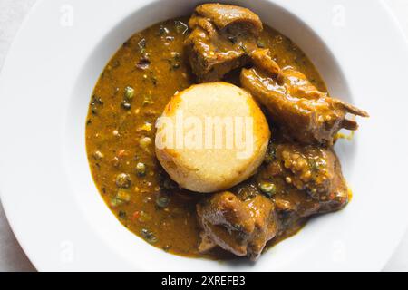 Blick von oben auf nigerianische Ogbono-Suppe und eba auf einem weißen Teller, Blick von oben auf Ogbono-Suppe mit garri und verschiedenen Fleischsorten auf einem Suppenteller Stockfoto