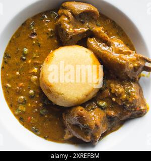 Blick von oben auf nigerianische Ogbono-Suppe und eba auf einem weißen Teller, Blick von oben auf Ogbono-Suppe mit garri und verschiedenen Fleischsorten auf einem Suppenteller Stockfoto