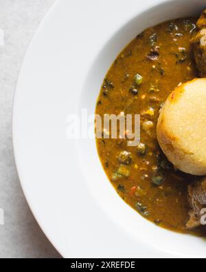 Blick von oben auf nigerianische Ogbono-Suppe und eba auf einem weißen Teller, Blick von oben auf Ogbono-Suppe mit garri und verschiedenen Fleischsorten auf einem Suppenteller Stockfoto