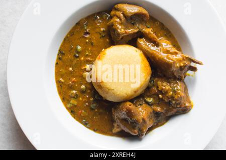 Blick von oben auf nigerianische Ogbono-Suppe und eba auf einem weißen Teller, Blick von oben auf Ogbono-Suppe mit garri und verschiedenen Fleischsorten auf einem Suppenteller Stockfoto