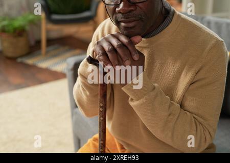 Älterer Afroamerikaner, der Holzstock hält und sitzt Stockfoto