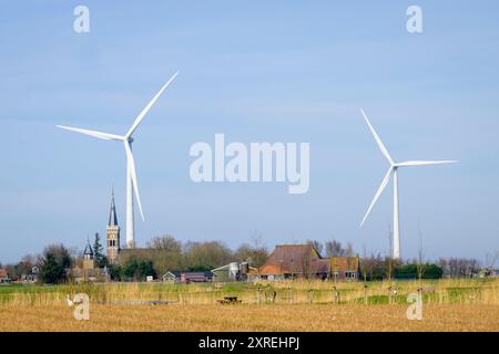 Moderne Windmühle für erneuerbare Energien, die über einer Altstadt mit einer alten Kirche thront, Niederlande. Stockfoto