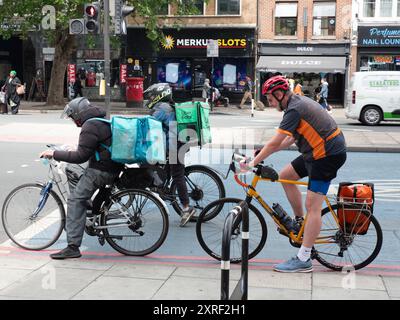 Deliveroo und Uber Eats Fahrradkuriere warten an der Ampel Stockfoto