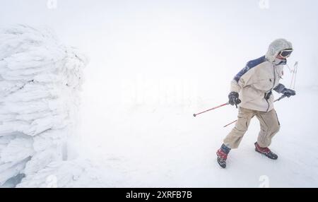 Hoverla, Ukraine - 10. März 2018: Bergsteiger mit Trekkingstöcken in den Karpaten im Winter. Der Mann klettert auf einen schneebedeckten Hügel. Hoverla Oberteil Stockfoto