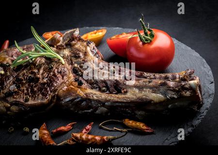 Köstliches Rindersteak mit Rosmarin, Chili Peeper und Tomaten auf Schieferbrett. Geröstetes Ribeye-Rindersteak mit Kräutern und Gemüse Stockfoto