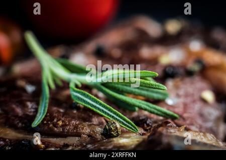 Rosmarinzweig auf gegrilltem Steak mit Gewürzen, Nahaufnahme. Saftig geröstetes Fleisch mit Rosmarin und Pfeffer Stockfoto