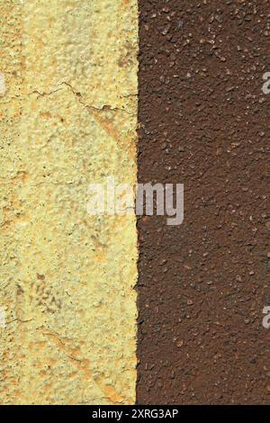 Eine alte Asphaltoberfläche, Hintergrund. Detaillierte Textur des dunkleren Bitumens in Nahaufnahme. Brauner Asphalt mit gelbem Teilstreifen. Rufenasphalt Stockfoto