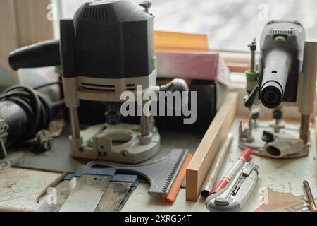 Nahaufnahme von Elektrowerkzeugen wie Bohrern, Sägen und Fräsern auf einer Holzwerkbank. Andere Schreinergegenstände und Zubehör, die im Hintergrund sichtbar sind Stockfoto