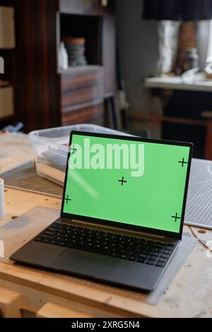 Laptop mit grünem Bildschirm auf einem Holzschreibtisch in einem modernen Arbeitsbereich mit Regalen mit Bürobedarf und Fenster im Hintergrund Stockfoto
