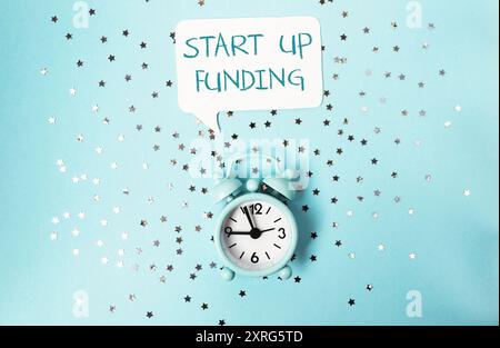 Eine Uhr mit den Worten „Start up funding“, die darüber steht. Die Uhr ist auf blauem Hintergrund mit einem Sternmuster Stockfoto