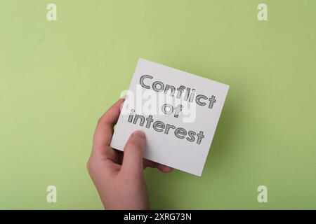 Eine Hand, die ein Blatt Papier hält, auf dem das Wort Interessenkonflikt steht. Das Konzept von Spannung und Unbehagen Stockfoto