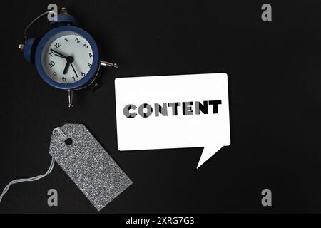 Ein blauer Wecker sitzt auf schwarzem Hintergrund und der Wortinhalt ist weiß geschrieben. Die Uhr ist von einem Tag umgeben, was ein Gefühl der Dringlichkeit verleiht Stockfoto