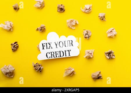 Korrigieren Sie Ihr Guthaben. Das Bild hat einen gelben Hintergrund mit einem weißen Schild, das auf Fix Your Credit steht. Es gibt viele Papierstücke, die um das sig verstreut sind Stockfoto