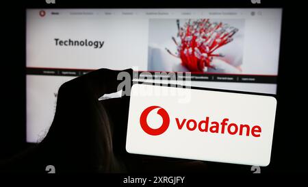 Person mit Smartphone und Logo des britischen Telekommunikationsunternehmens Vodafone Group plc vor der Website. Schwerpunkt auf dem Display des Telefons. Stockfoto