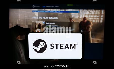 Person, die ein Mobiltelefon mit dem Logo des US-amerikanischen Videospielvertriebs Steam (Valve) vor der Unternehmenswebseite hält. Schwerpunkt auf dem Display des Telefons. Stockfoto