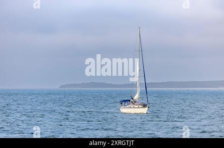 Kleines Segelboot mit einem Mann, der an einem Segel in der Gardiners Bay arbeitet Stockfoto