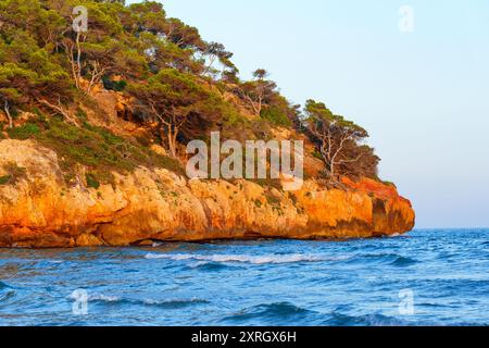 Goldene Klippen steigen von den sanften Wellen des Meeres auf, beleuchtet vom sanften Licht des Sonnenuntergangs in Tarragona, Katalonien. Stockfoto