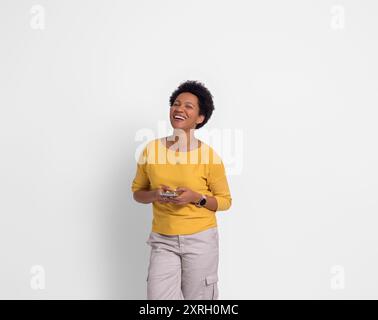 Fröhlich schöne Frau mit Afro-Haaren Nachrichten über Handy und lachen auf weißem Hintergrund Stockfoto
