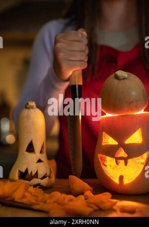 Mädchen macht eine Halloween-Dekoration, feiert Halloween zu Hause und bereitet Kürbisse düstere Atmosphäre und beleuchteten Kürbis vor. Stockfoto