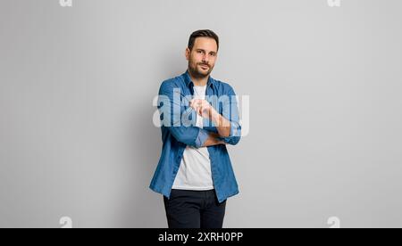 Porträt eines selbstbewussten charmanten Geschäftsmannes, der eine Brille hält und ernsthaft auf grauem Hintergrund posiert Stockfoto