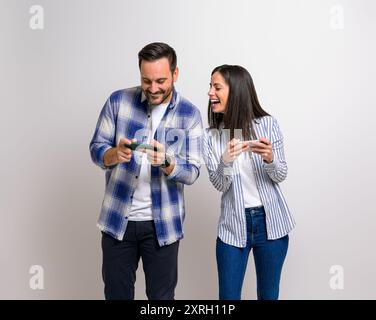 Junge Freundin, die Videospiele spielt und fröhlich auf das Handy des Freundes schaut. Aufregendes Paar, das Spaß am Spielen hat und sich gegenseitig antritt Stockfoto