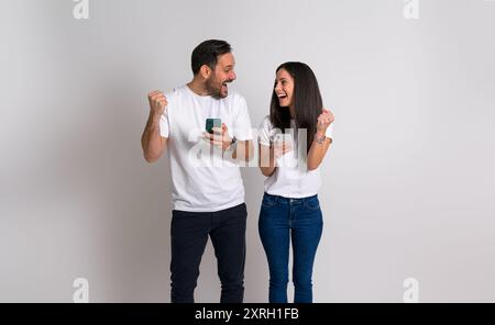 Ein junges Paar pumpt Fäuste und schrie aufgeregt, nachdem es Nachrichten über das Smartphone erhalten hat. Ekstatischer Mann und Frau, die sich glücklich anschauen Stockfoto
